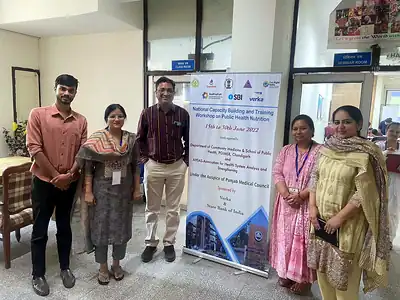 Five attendees beside National Capacity Building and Training Workshop on Public Health Nutrition standee