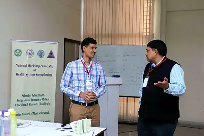 Two facilitators discussing beside workshop banner and whiteboard at 2nd NWHSS 2016, PGIMER Chandigarh