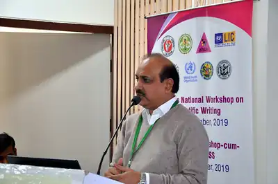 Speaker at microphone beside workshop banner, scientific writing workshop December 2019